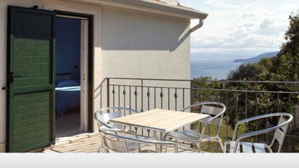 Un balcón con una mesa, sillas, una puerta y vista al mar.
