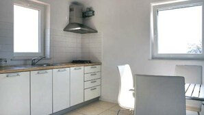Una cocina moderna con armarios blancos, una campana extractora de acero inoxidable y dos ventanas que aportan luz natural.