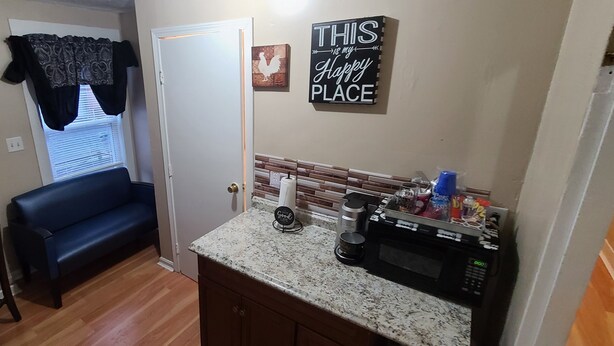 A compact kitchen with a microwave, coffee maker, and various kitchen items on the counter. A blue couch and a dining table with a checkered tablecloth are in the adjacent living area.