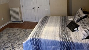 A bedroom with a bed, a radiator, a door, and a small picture frame on the wall.