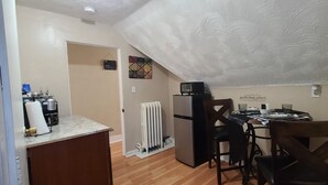 A compact kitchen with a refrigerator, a coffee maker, and a dining table with chairs.