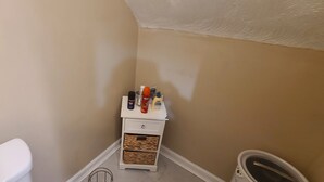 A corner of a room with a white dresser, a trash can, and a white toilet.