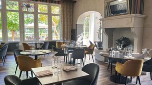 Un restaurante con varias mesas y sillas, amplias ventanas con vistas a árboles y una chimenea.