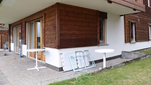En stuga byggd av trä med en inglasad veranda, ett litet bord och en stol.