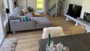 Una sala moderna con un sofá seccional gris, un televisor de pantalla plana, una escalera y vistas al exterior.