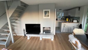 Una sala moderna con televisor de pantalla plana, chimenea, escalera y zona de cocina con taburetes de bar.