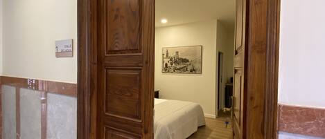 A hotel room with a bed, a painting on the wall, and a wooden door.