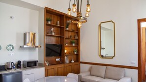 A modern kitchen with a built-in microwave, a coffee maker, and a dishwasher. There is a round dining table with chairs, a beige sofa, and a large mirror on the wall. - Nava Suites (San Cristóbal de La Laguna)