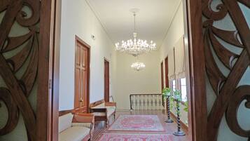 A hallway with a chandelier, wooden doors, a bench, and a patterned rug.