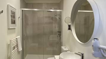 Un baño moderno con ducha de vidrio, un lavamanos blanco y un espejo redondo.
