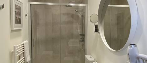 A modern bathroom with a glass-enclosed shower, a white sink, and a round mirror.