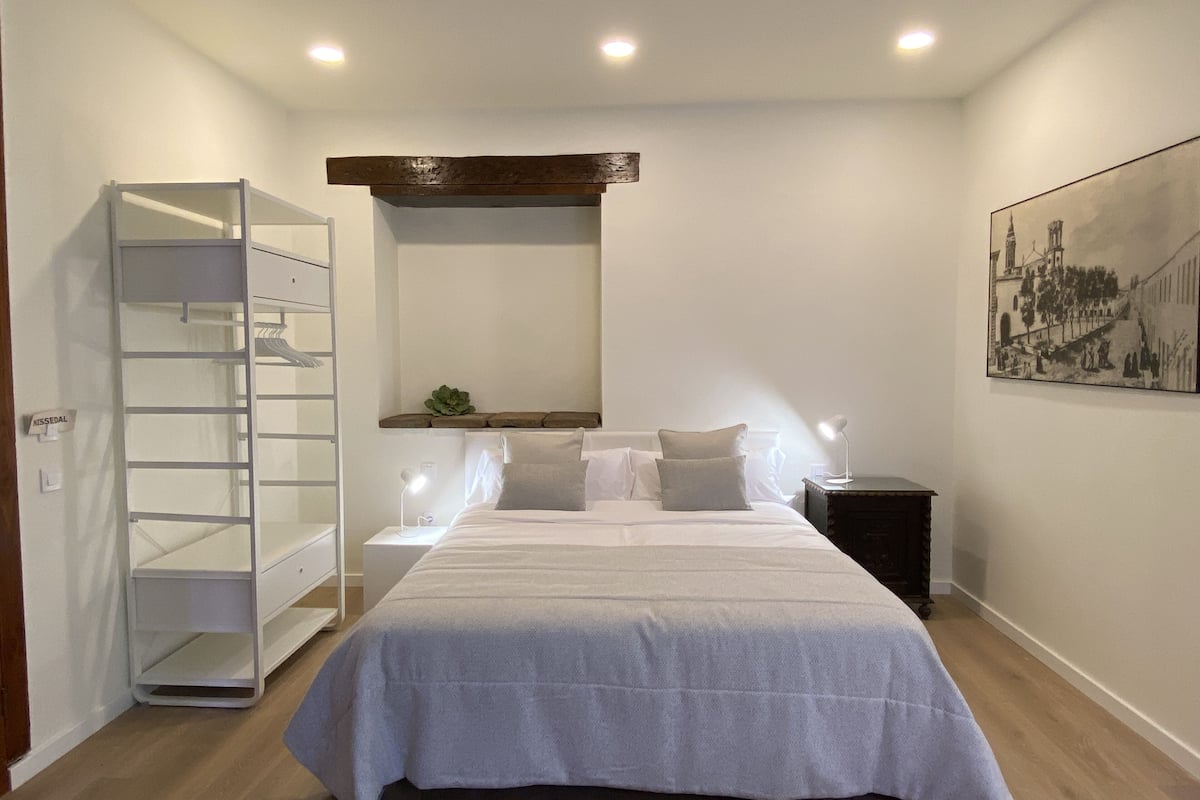 Een slaapkamer met een bed, een nachtkastje, een lamp, een kledingkast en een schilderij aan de muur.