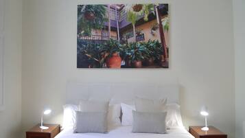 A hotel room with a bed, two bedside tables, a headboard, and a large picture of a courtyard with plants and a building.