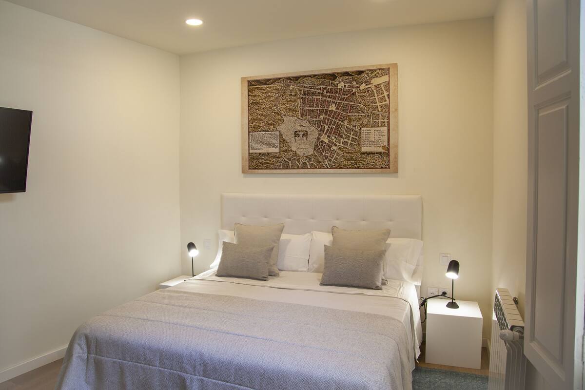 Een slaapkamer met een groot bed, twee nachtkastjes, een wandtelevisie en een kaartwerkje boven het bed.