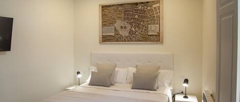 Un dormitorio con una cama grande, dos mesitas de noche, un televisor instalado en la pared y una obra de arte con un mapa sobre la cama.
