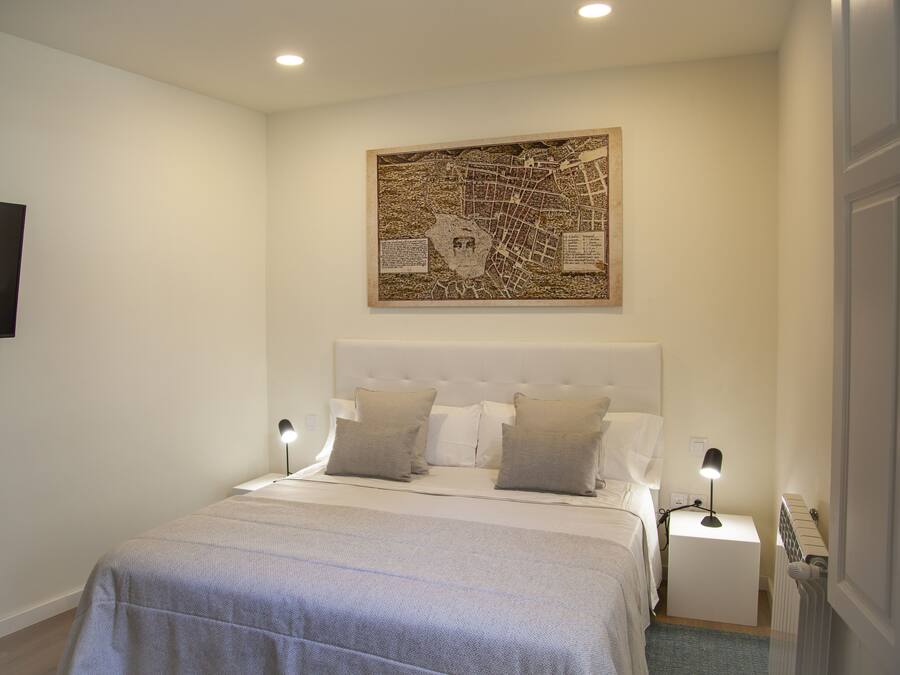 Une chambre avec un grand lit, deux tables de chevet, un téléviseur fixé au mur et une œuvre d’art représentant une carte au-dessus du lit.