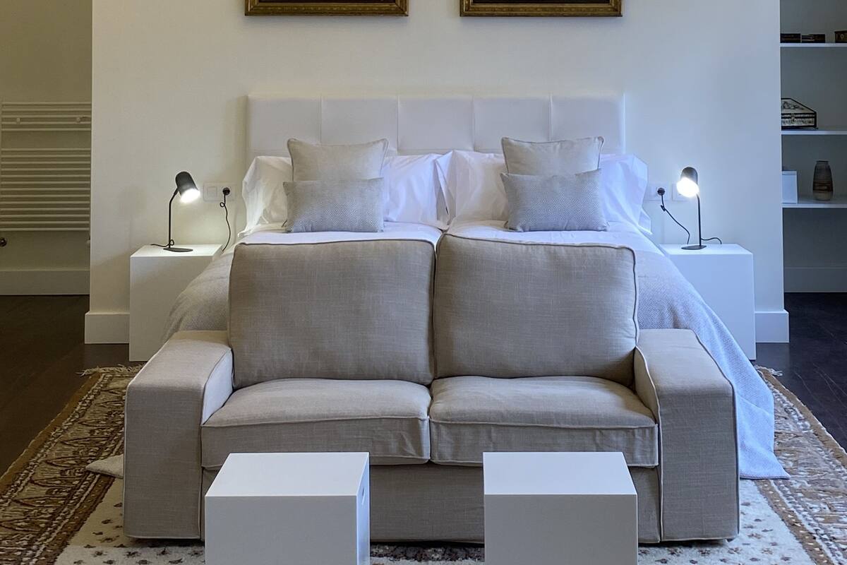 Een slaapkamer met een groot bed, twee nachtkastjes met lampen, een kroonluchter en twee ingelijste foto's aan de muur.
