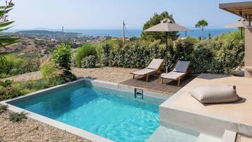 Ein rechteckiger Pool mit Holzterrasse, zwei Liegestühlen und einem Sonnenschirm.