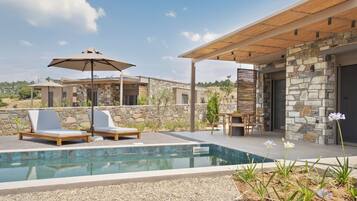 Ein moderner Poolbereich im Freien mit Liegestühlen, einer Pergola und einem Steinhaus.