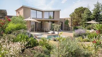 Una casa moderna con piscina, rodeada de diversas plantas y árboles.