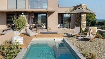 A modern house with a swimming pool, outdoor seating, and a view of the sea.