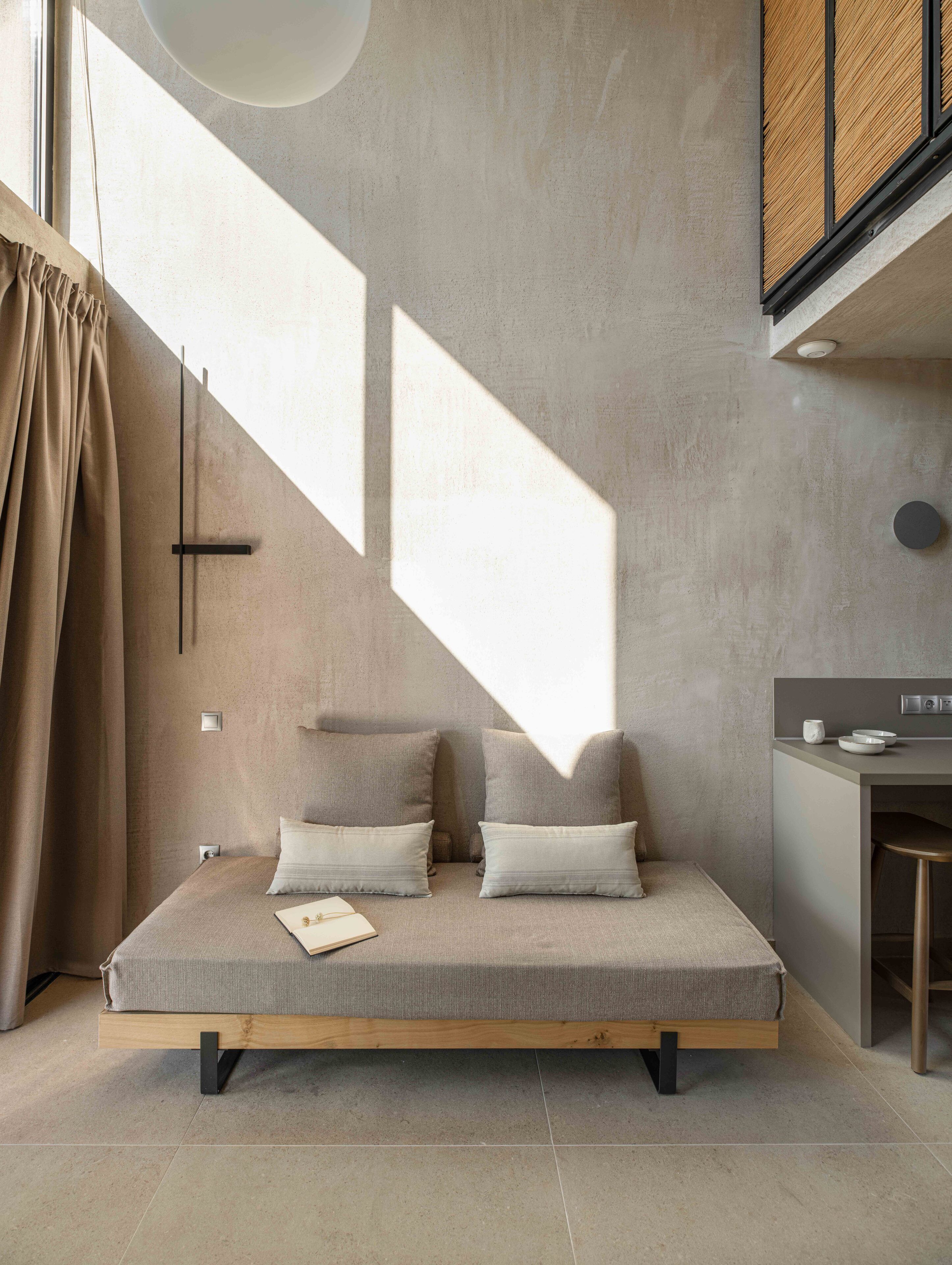 Una habitación moderna de diseño minimalista, con un sofá cama con cojines, una mesita y una cocina que incluye una encimera y taburetes.