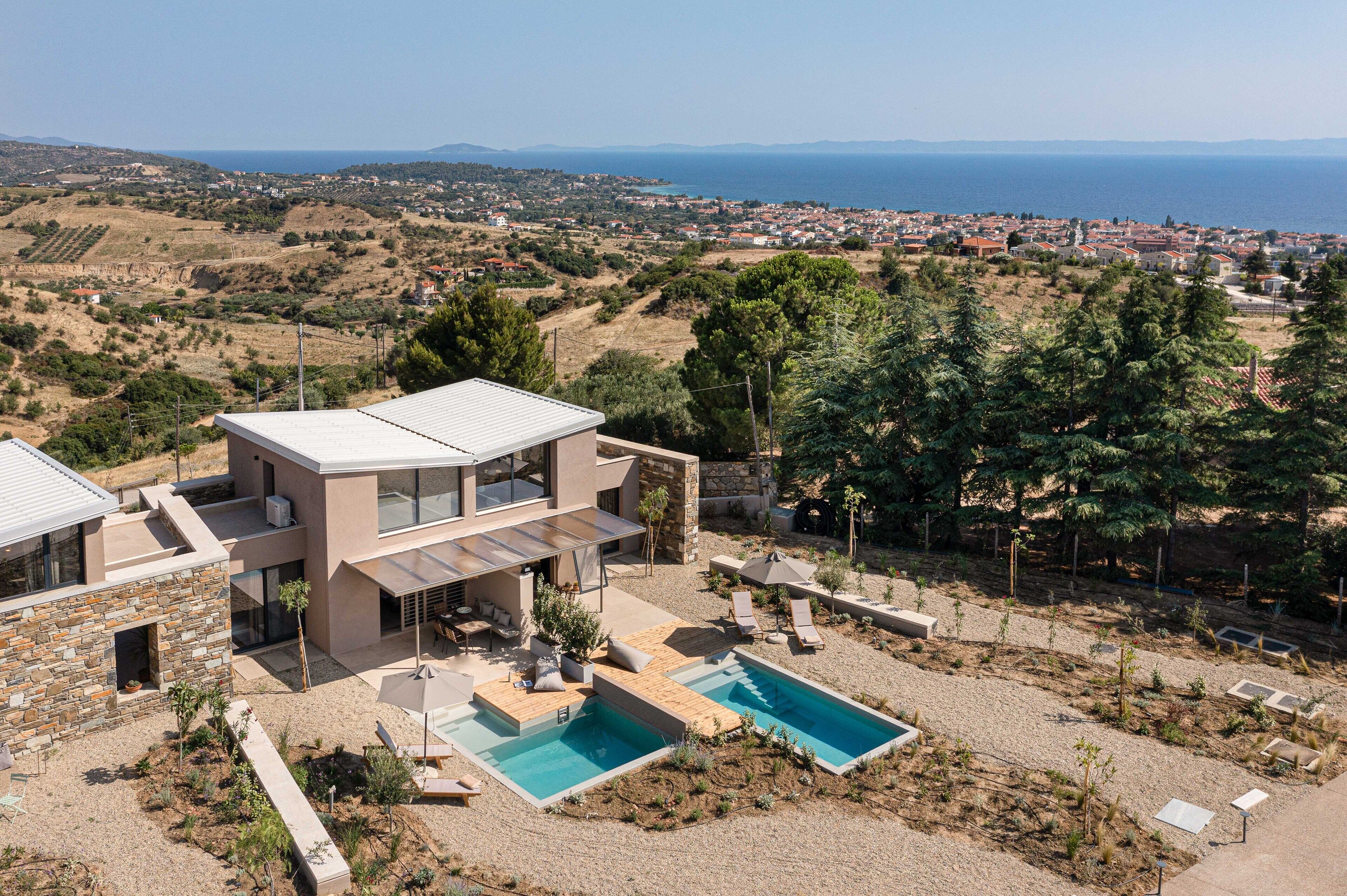 Et moderne hus med pool, udendørs møbler og udsigt til havet og bakker.