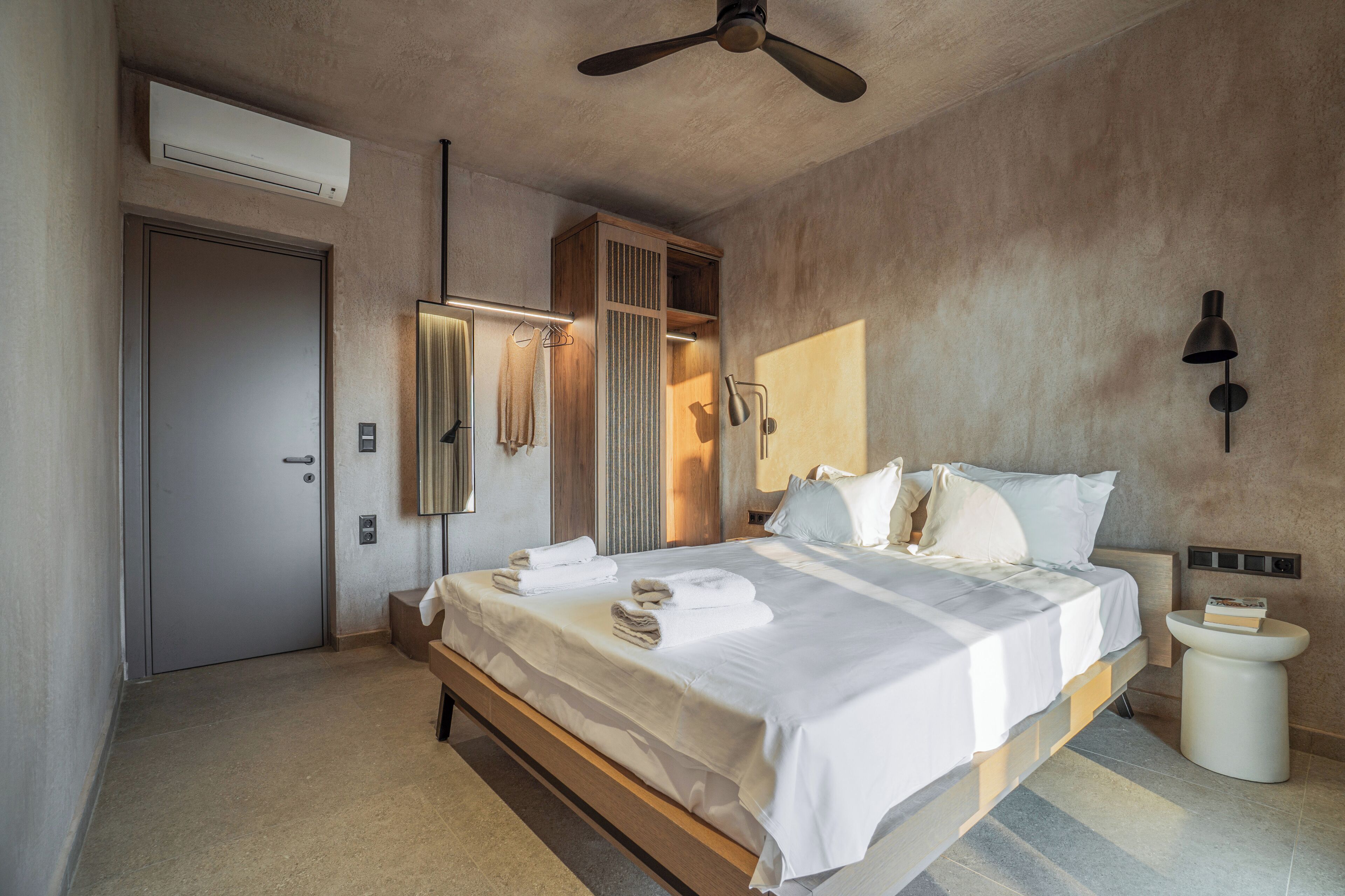Una habitación de hotel moderna con una cama grande, un ventilador de techo, un equipo de aire acondicionado, una mesita de noche y un armario empotrado.
