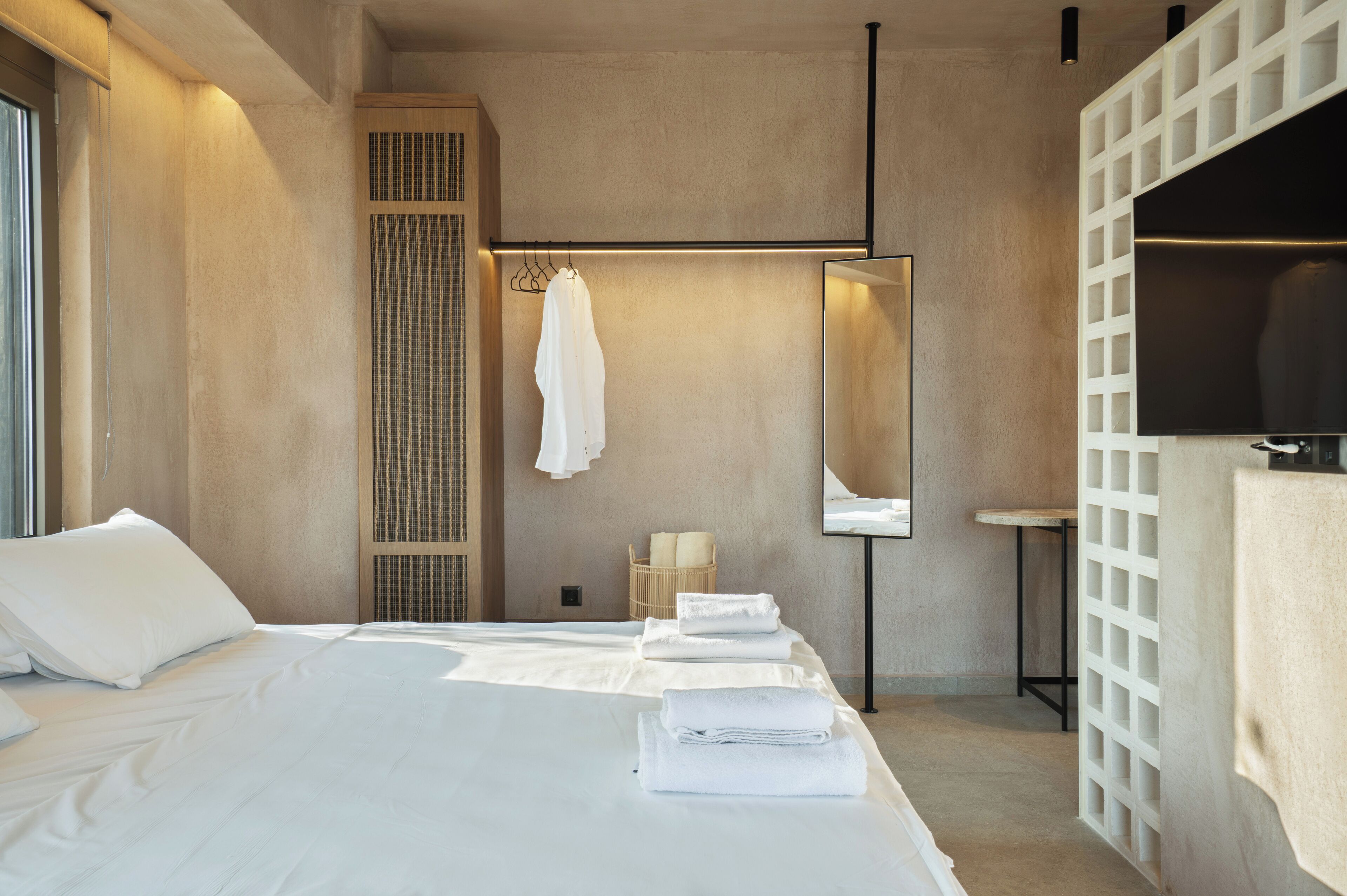 A modern hotel room with a large bed, a hanging robe, a mirror, and a small table.