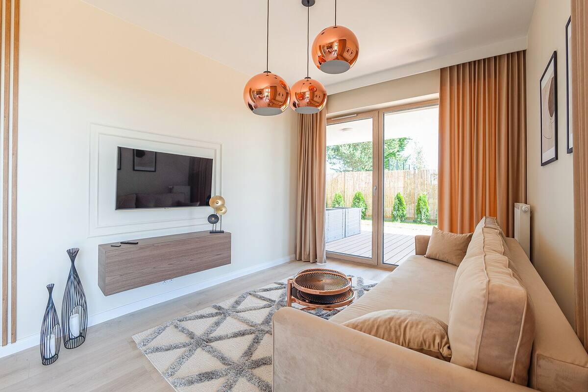 A modern living room with a sofa, a TV mounted on the wall, and a large window with curtains.