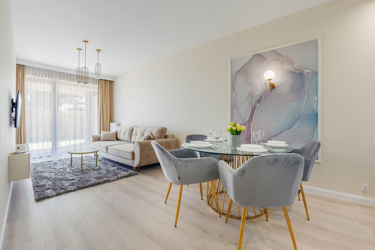 A modern living room with a dining area, featuring a sofa, a glass dining table with chairs, and a large abstract painting on the wall.