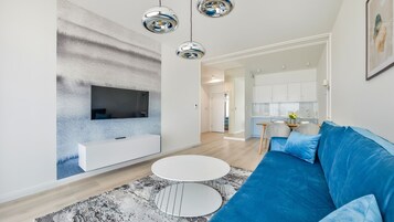 Ein modernes Wohnzimmer mit einem blauen Sofa, einem weißen Couchtisch und einem an der Wand befestigten Fernseher.