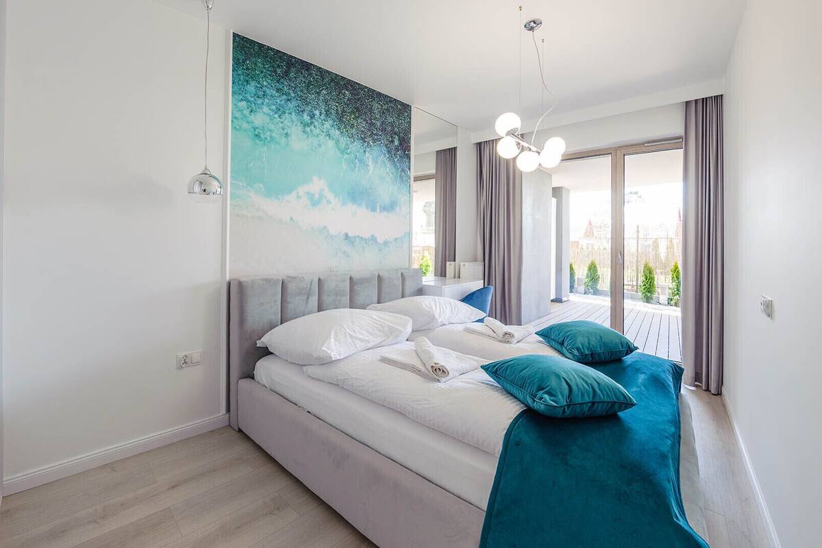 A modern bedroom with a large bed, a view of the outdoors, and a ceiling light fixture.