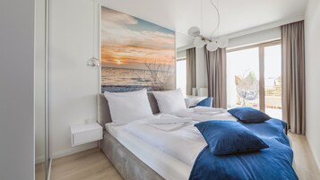 Una habitación de hotel moderna con una cama grande, vistas al mar a través de la ventana y una lámpara en el techo.