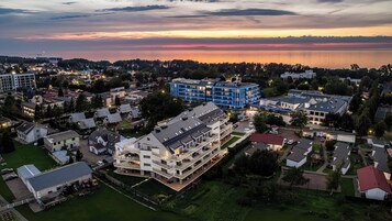 Vista aérea de una zona residencial con edificios modernos, incluyendo una estructura azulada destacada, rodeada de vegetación y con vista al agua.