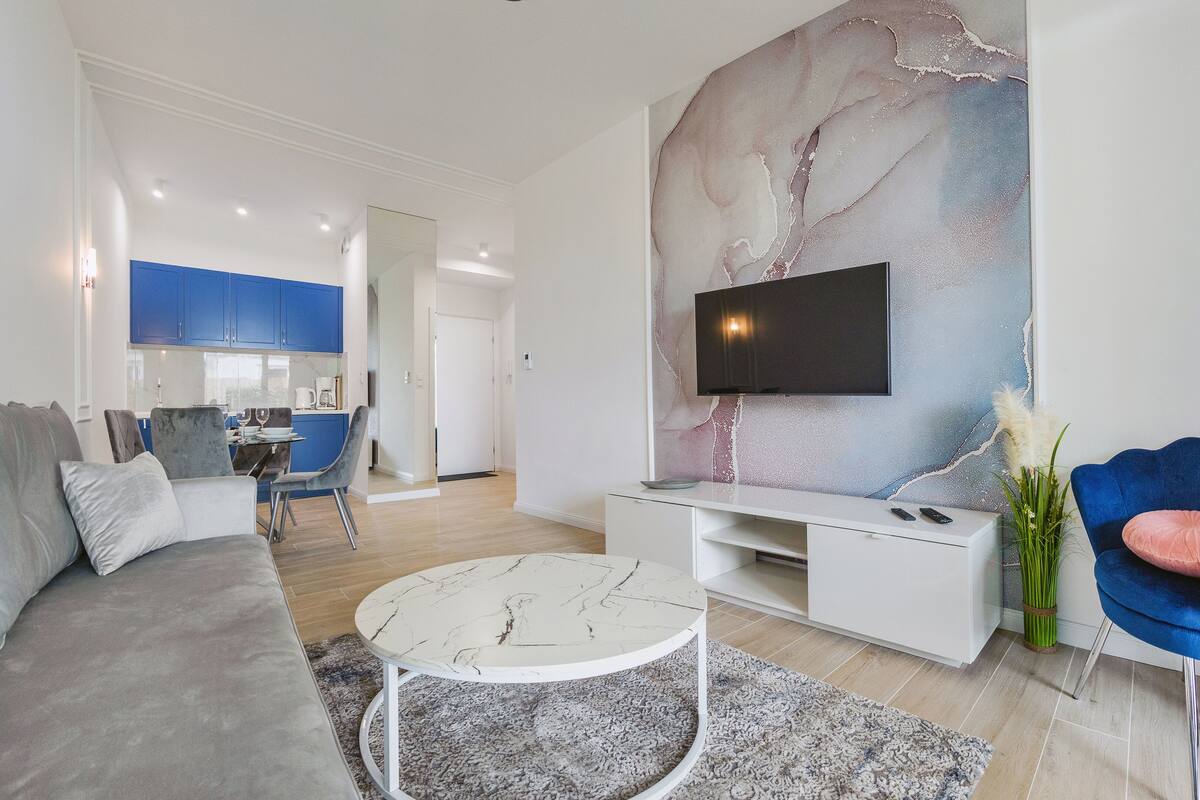 A modern living room with a marble-patterned wall, a flat-screen TV, a grey sofa, a blue armchair, and a round coffee table.