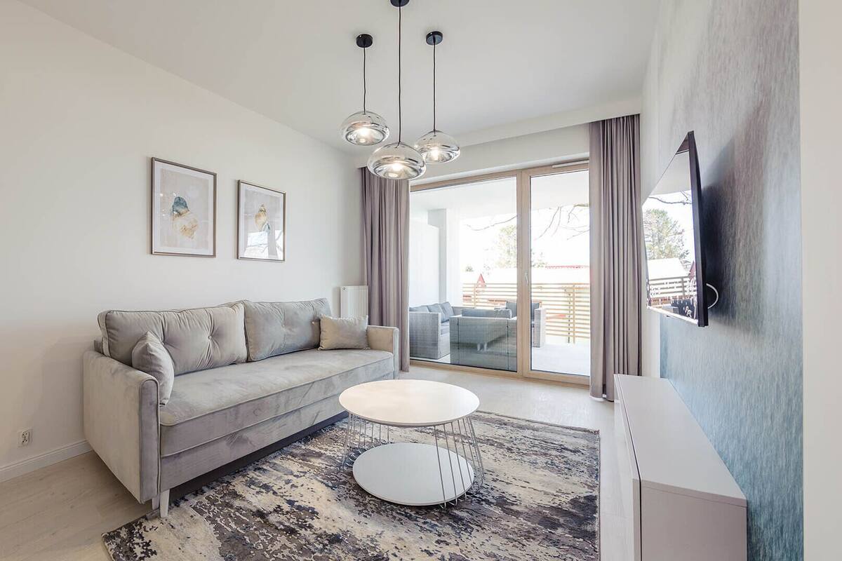A modern living room with a grey sofa, a round coffee table, and a large window with a view of the outdoors.