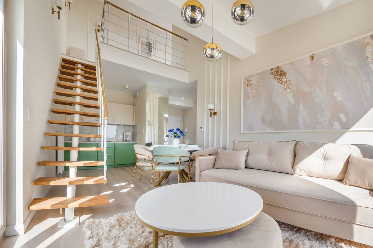 A modern living room with a staircase, a round white coffee table, a beige sofa, and a large abstract painting.