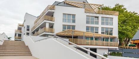 A modern multi-story building with a staircase leading to the upper floors, large windows, and a flat roof.