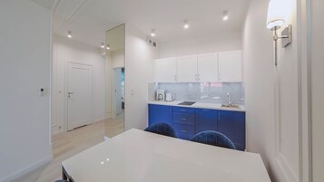 Una cocina compacta con armarios blancos, una encimera azul y una mesa de comedor blanca.