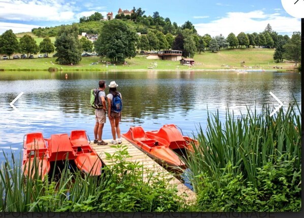 Eine Holzsteganlage mit roten Booten, ein See und eine Burg im Hintergrund.