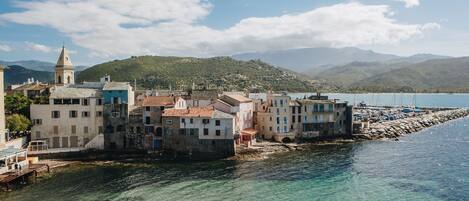 A coastal town with buildings along the waterfront, clear water, and mountains in the background.