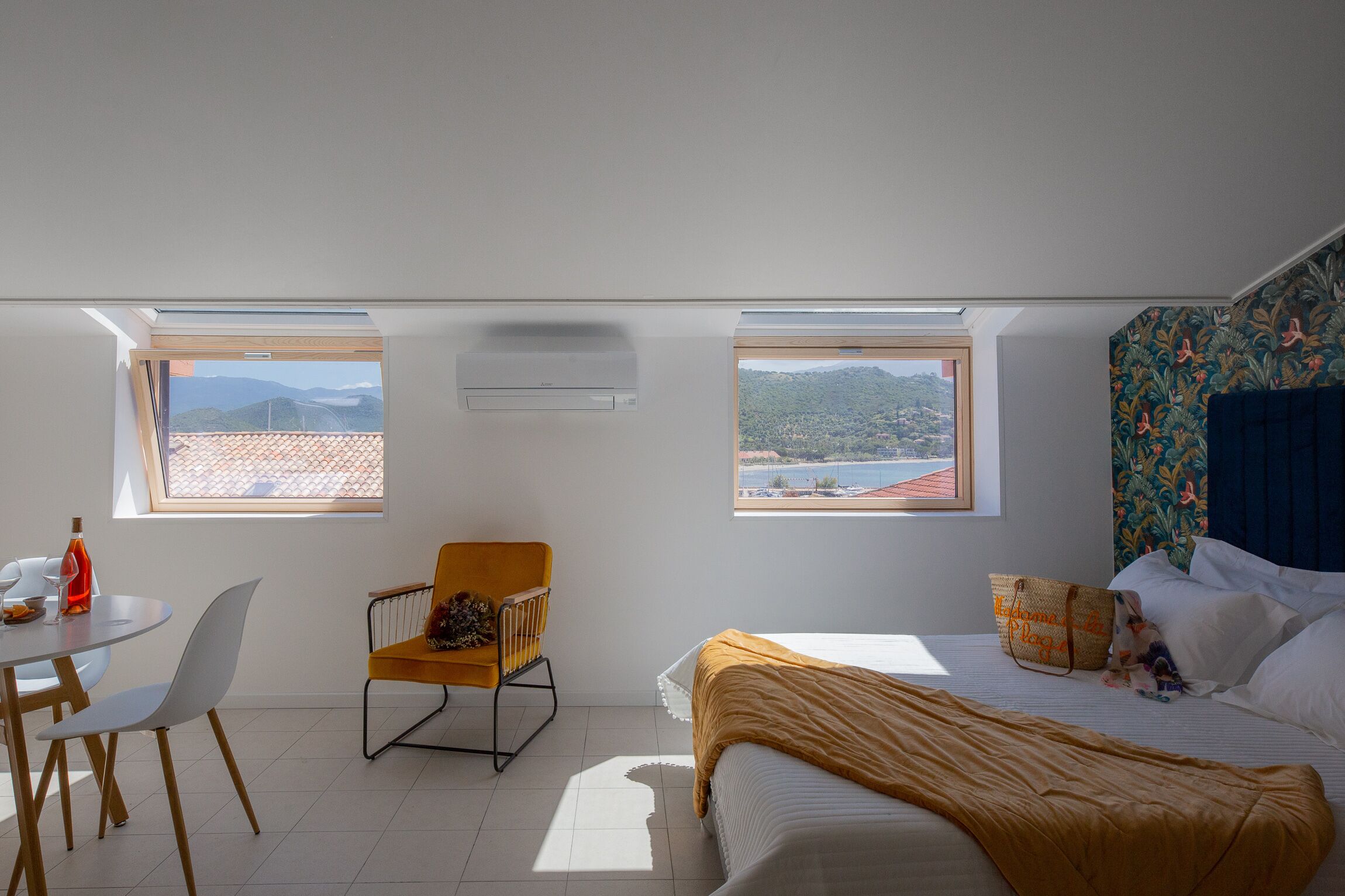 Quarto com duas claraboias, uma cama, uma cadeira, uma mesa e vista para as montanhas.