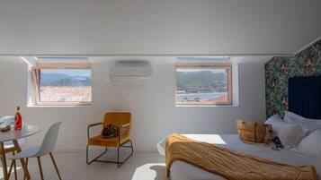 Quarto com duas claraboias, uma cama, uma cadeira, uma mesa e vista para as montanhas.