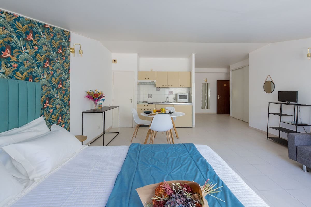 A modern hotel room with a bed, a small kitchenette, a dining area, and a living area.