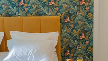 Habitación de hotel con cama, una mesita redonda con una bebida y pared con papel tapiz tropical.