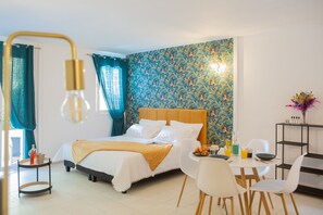 A hotel room with a bed, breakfast table, chairs, and a wall with a floral pattern.