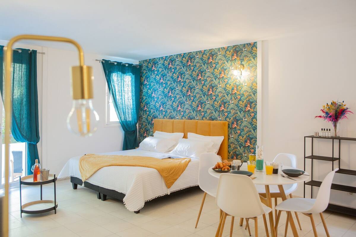 A hotel room with a bed, breakfast table, chairs, and a wall with a floral pattern.