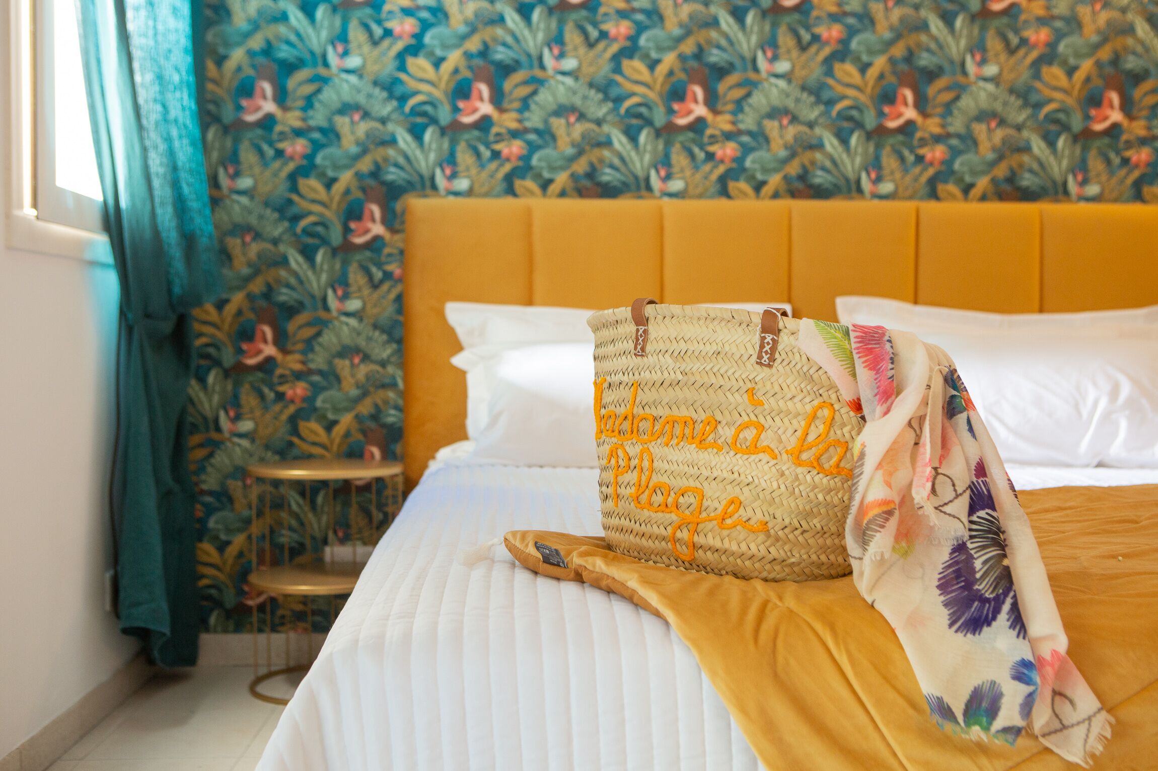 Ein Bett mit gelbem Kopfteil, ein gewebter Korb mit Schriftzug und eine gesteppte Decke mit Blumenmuster.