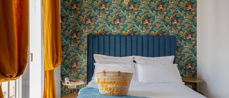 A bedroom with a blue headboard, a bed with white linens, a blue blanket, and a woven basket with text on it.